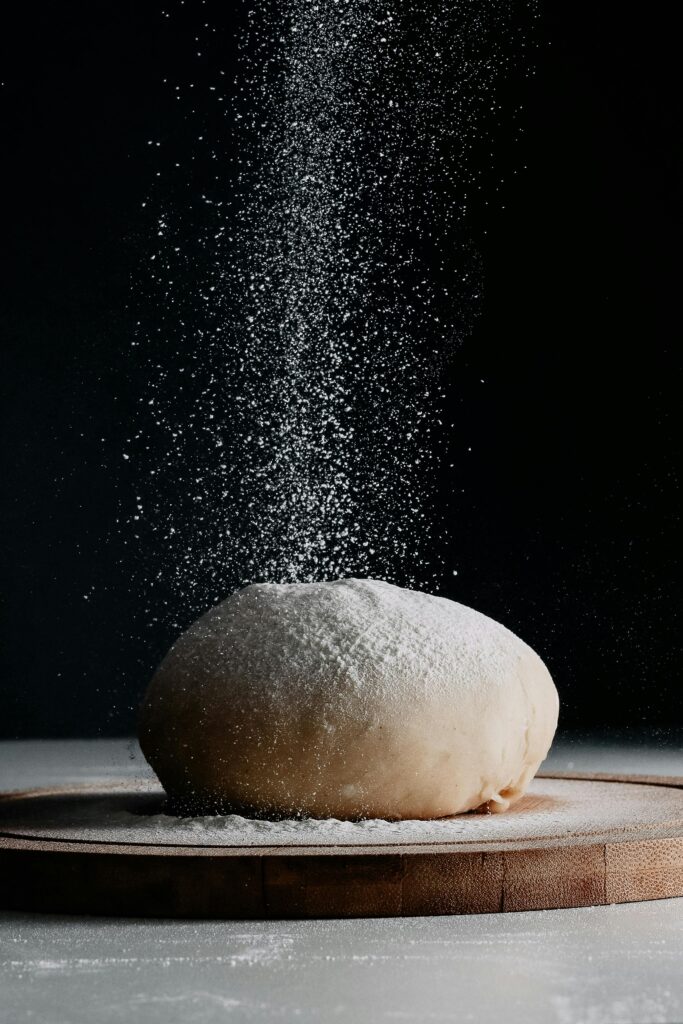 Captivating image of dough on a board as flour gracefully falls, highlighting baking creativity.