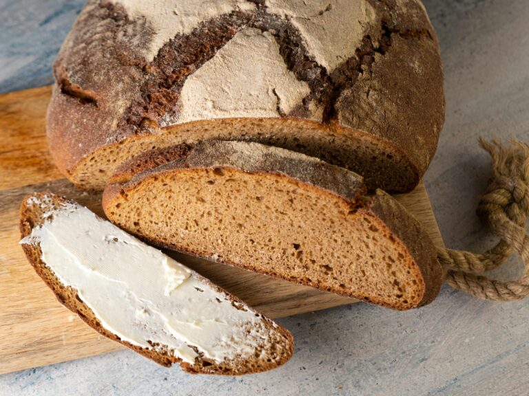 Sliced rustic loaf of bread with buttered piece on a wooden cutting board.